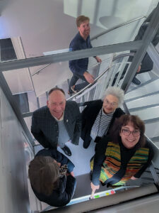 2. Bürgermeister Günter Eibl und Spenderin Traudl Bergau fahren zusammen beim Pressetermin mit Vorsitzender Dr. Sybille Krafft und einer Journalistin ins Obergeschoss.